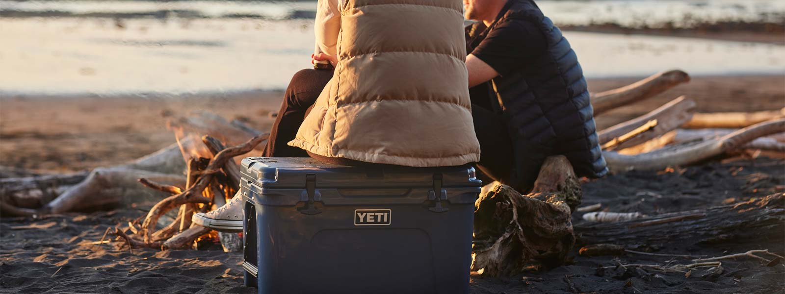 Two people sitting on a yeti cooler at the beach